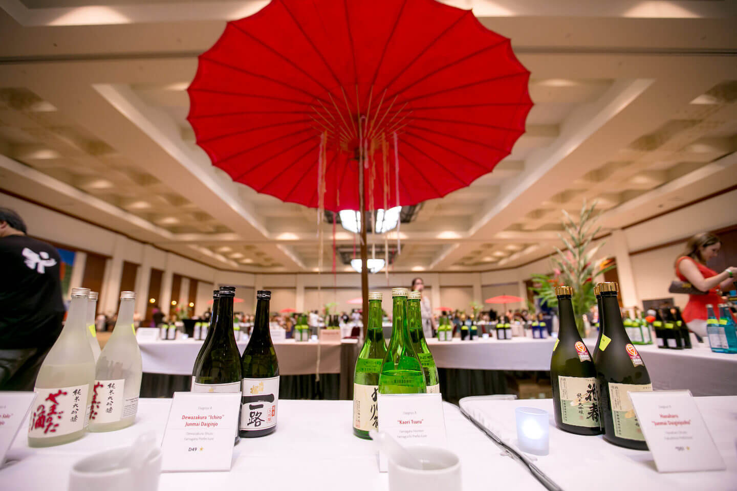 Sake bottles on the table with a large Japanese red umbrella behind inside of a ballroom (2015 Honolulu)