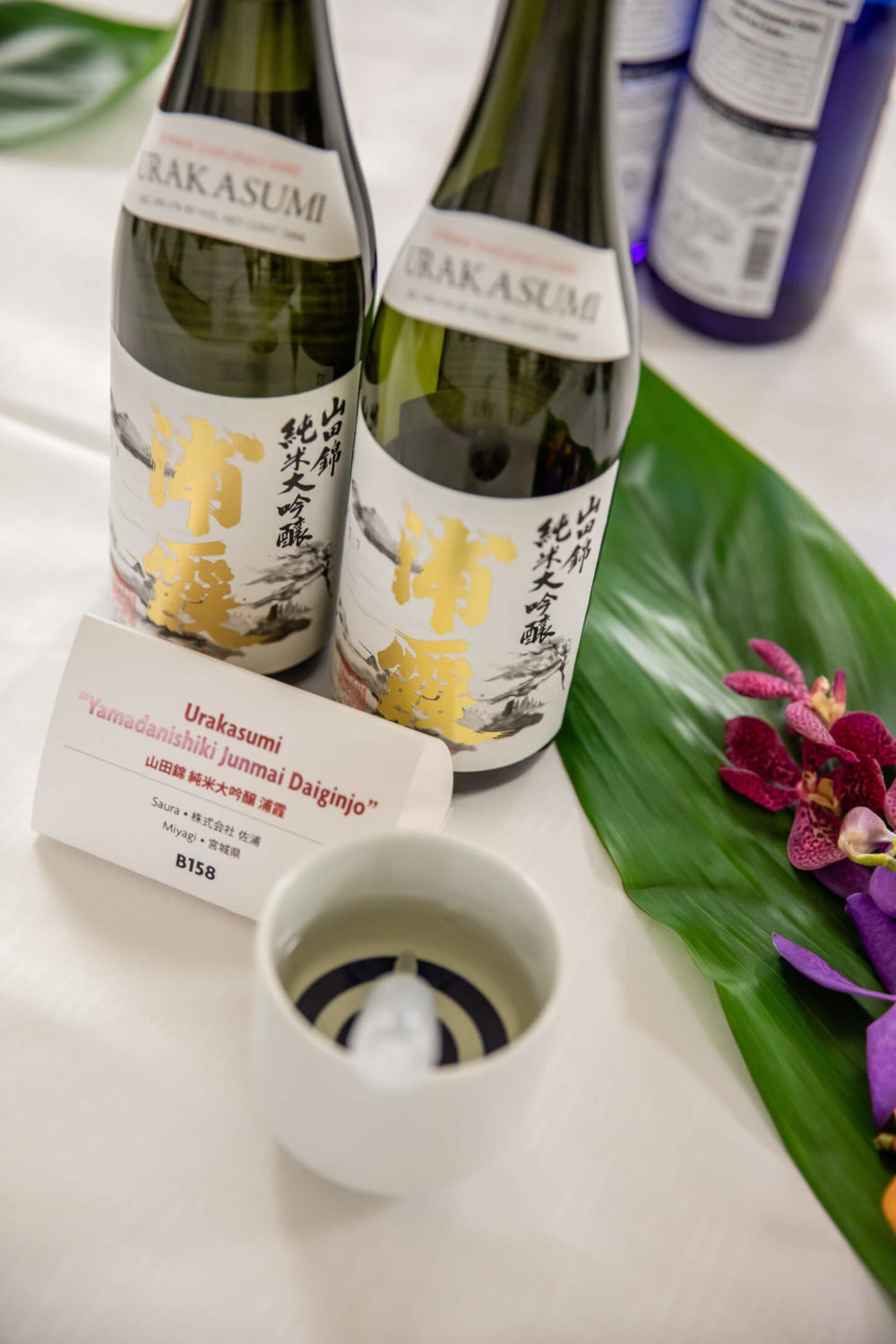 jos19tk251 Bottles, a janome cup, a pippette, sake card, ti leaves and orchids on the table (2019 Tokyo)